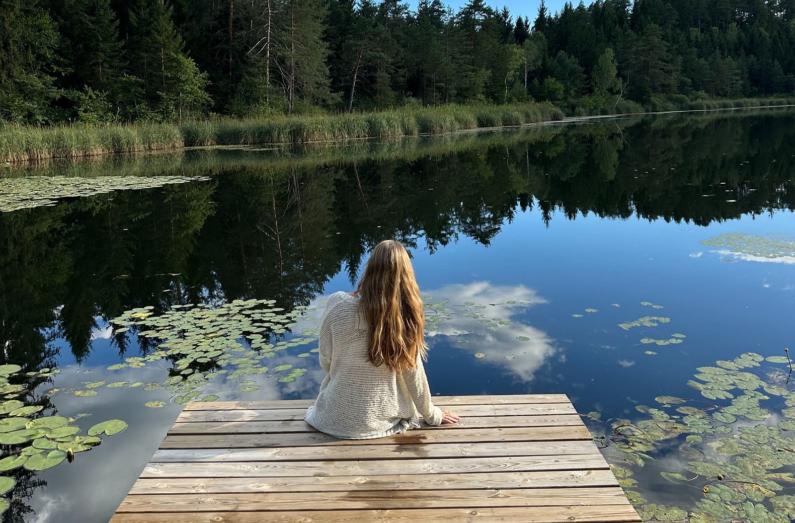 Girl sitting at a body of water, reflecting.